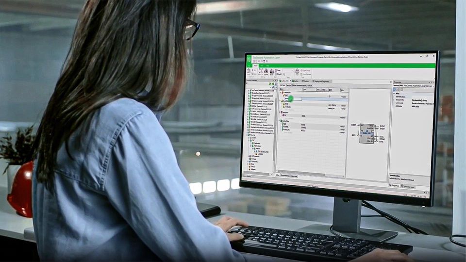 woman with long gray hair and glasses working at a computer station on a factory floor
