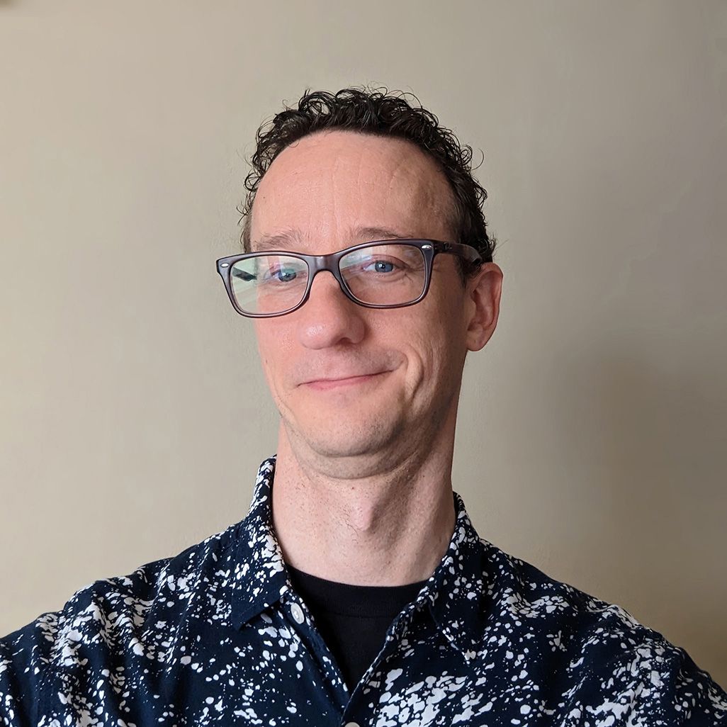 headshot of middle-aged, white cisgender male with glasses and curly hair.