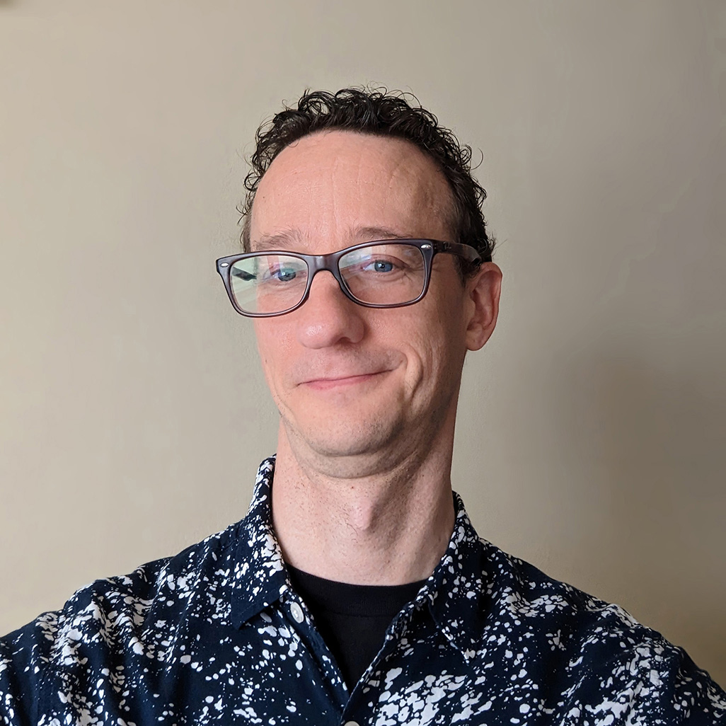 headshot of middle-aged, white cisgender male with glasses and curly hair.